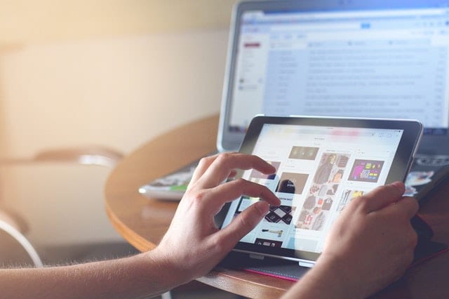 person on tablet with laptop in the background